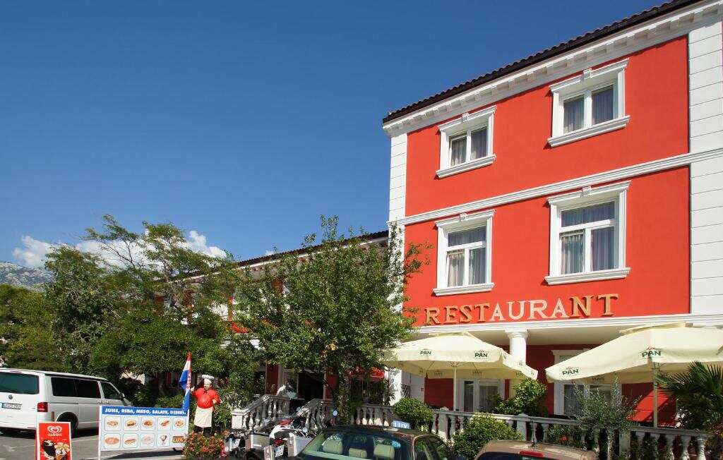 The red facade of Lux Hotel Pansion with its restaurant terrace in Jablanac